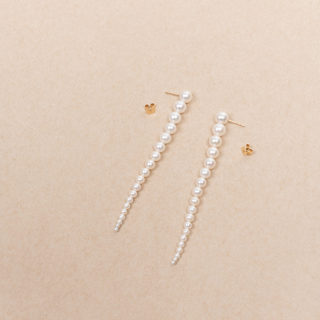 The Sienna Grand Earrings by Sophie Bille Brahe are a stunning and dramatic pair of earrings crafted in 14K yellow gold and white freshwater pearls graduating in size, which elegantly drop down