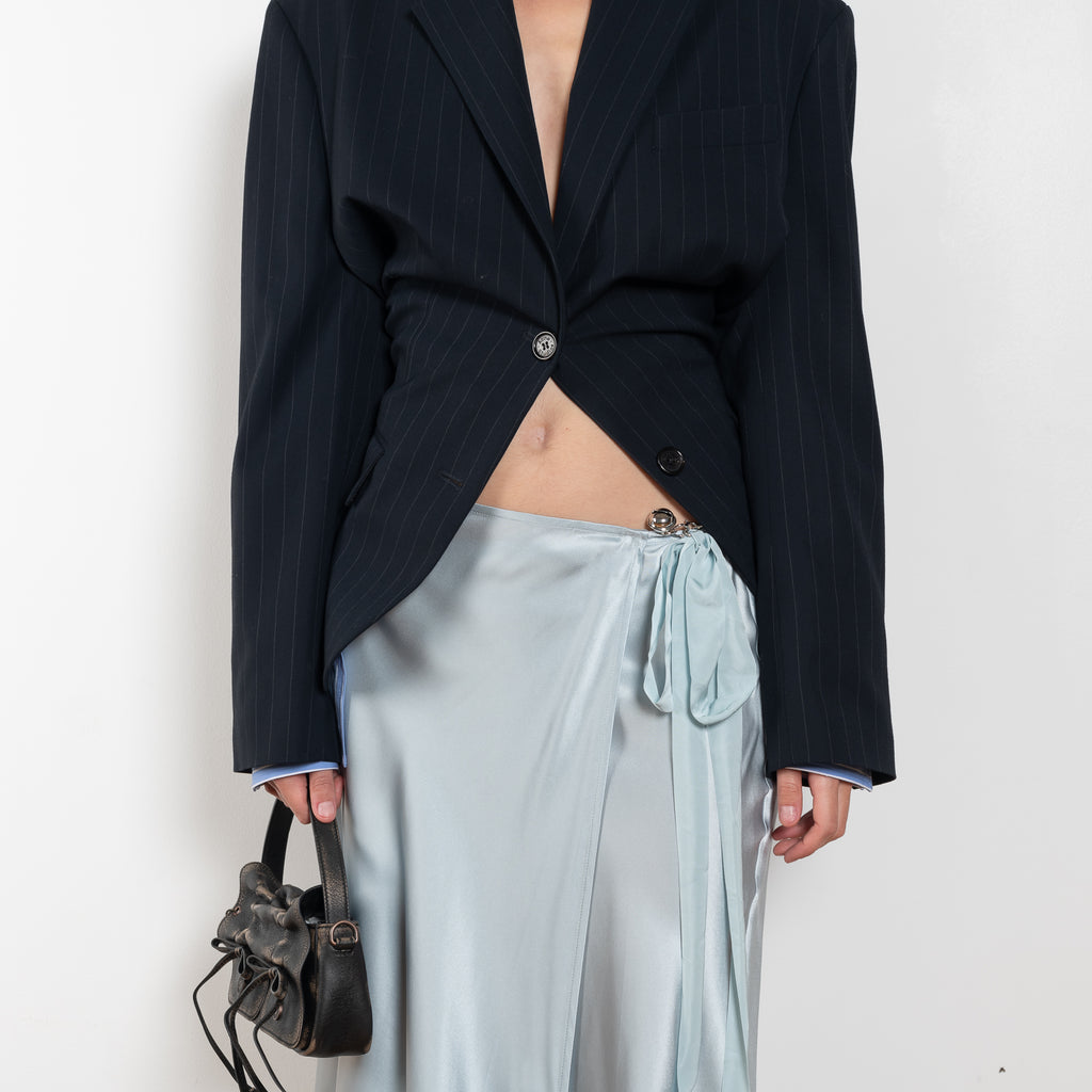The Silk Wrap Skirt by Acne Studios is a silk A-line skirt with a wrap construction, featuring silver-toned bell and hardware details with a tonal tie-up closure