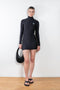 The High Neck Mini Dress by Coperni is a signature fitted mini dress in black with a silver C Logo on the chest and thumb holes
