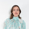 The Tracy Silk Blouse by Julie Kegels is a silk wrap top in aqua with a Hawaïan floral print and contrasting cuffs