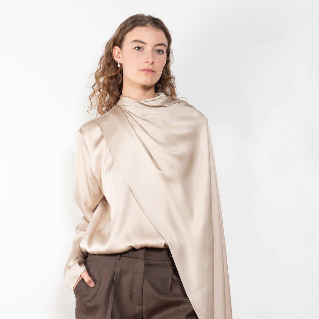 The Silk Shirt by Magda Butrym is a long-sleeve silk blouse with a round neck and carefully draped fabric that gives way to a dramatic cape that sweeps off the shoulder