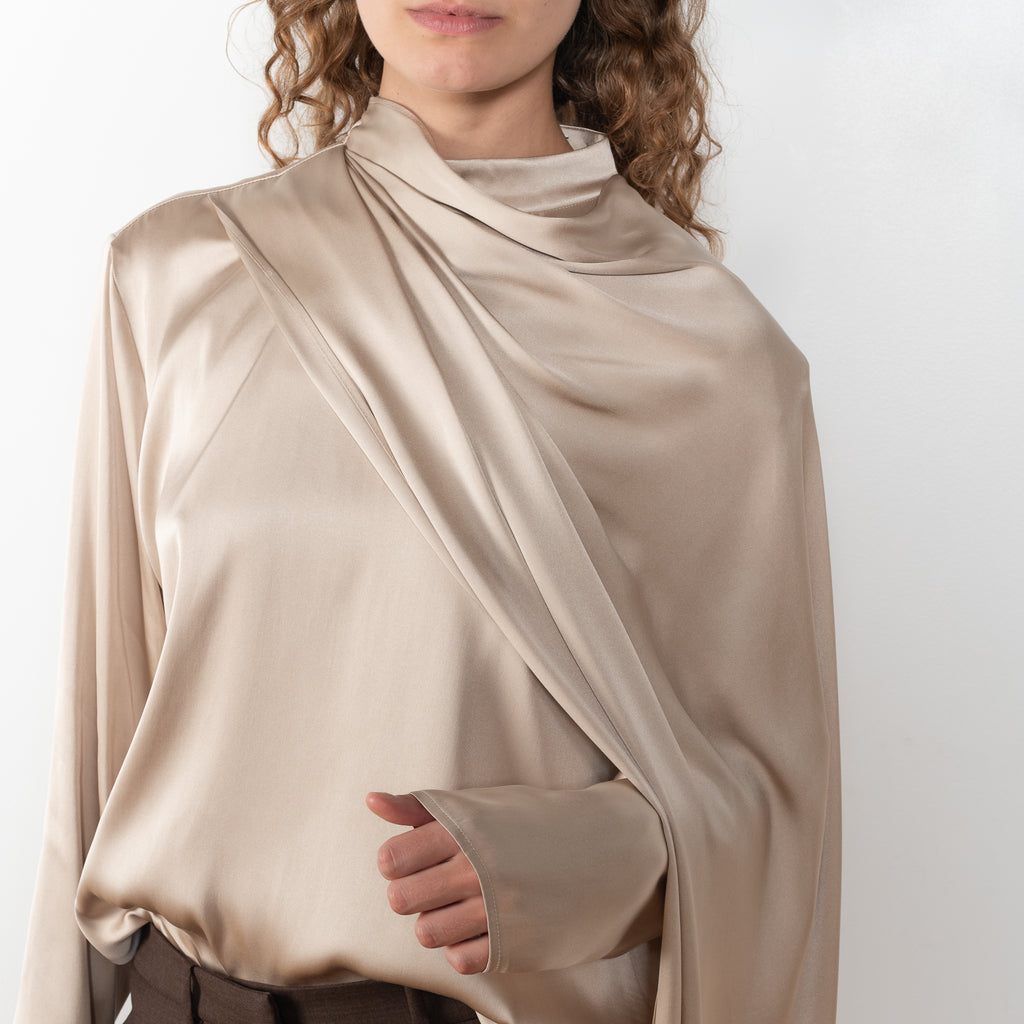 The Silk Shirt by Magda Butrym is a long-sleeve silk blouse with a round neck and carefully draped fabric that gives way to a dramatic cape that sweeps off the shoulder