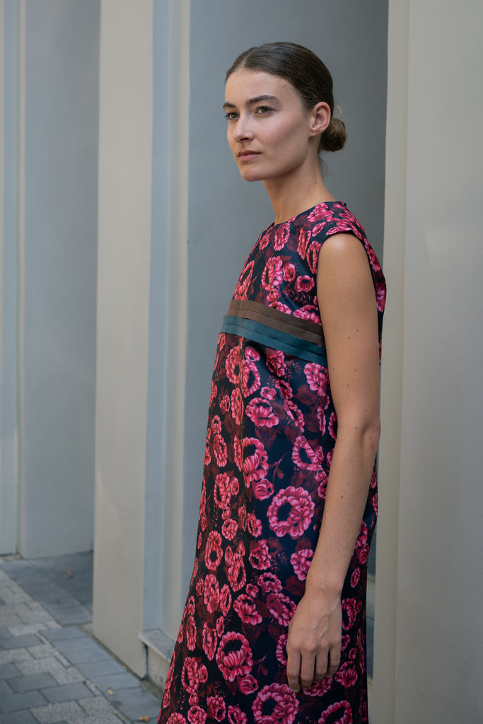 The Long Shift Dress by Meryll Rogge is a sleeveless shift dress crafted in floral scuba satin, featuring a round neckline and a contrasting ribbon detail.