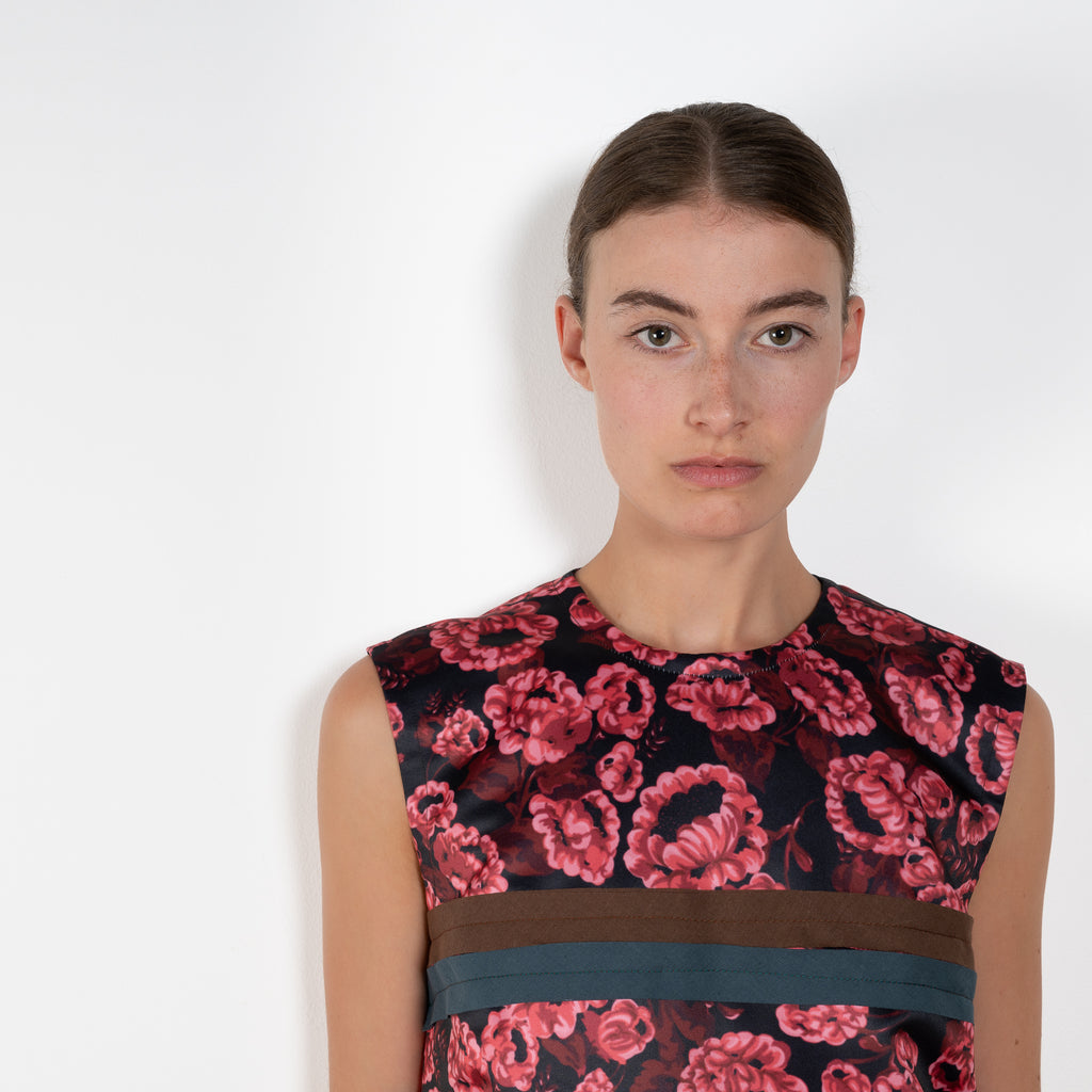 The Long Shift Dress by Meryll Rogge is a sleeveless shift dress crafted in floral scuba satin, featuring a round neckline and a contrasting ribbon detail.