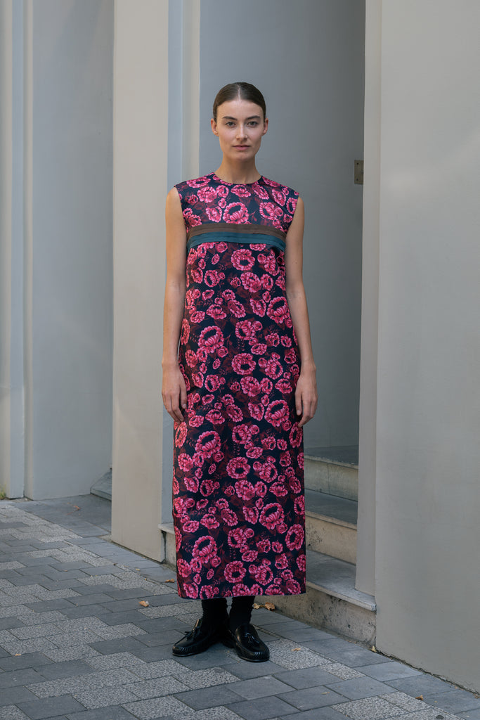 The Long Shift Dress by Meryll Rogge is a sleeveless shift dress crafted in floral scuba satin, featuring a round neckline and a contrasting ribbon detail.