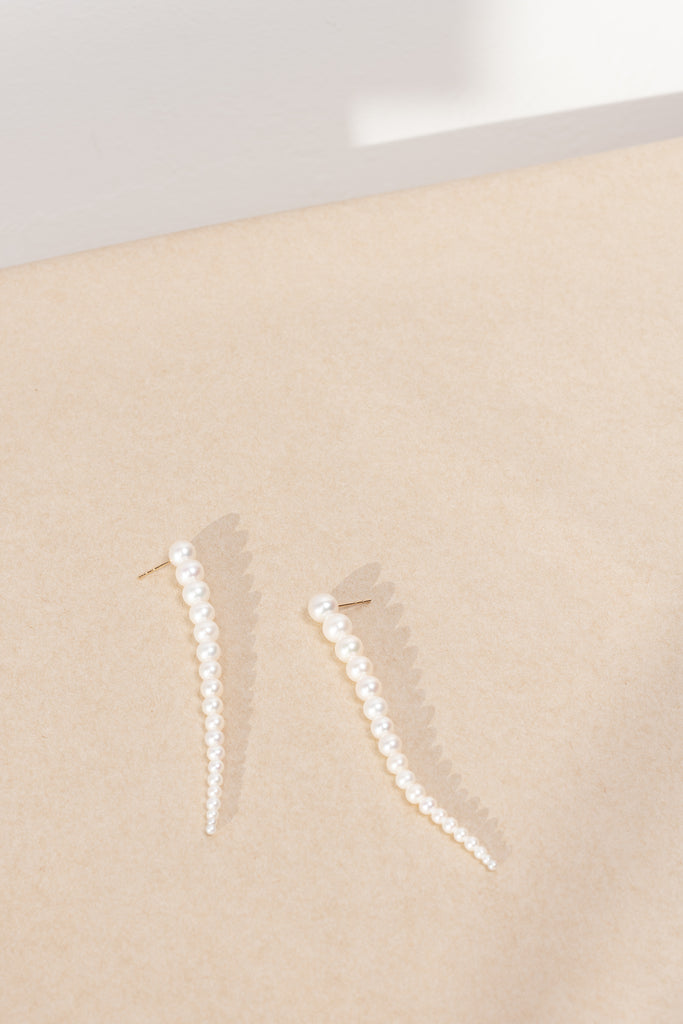 The Sienna Grand Earrings by Sophie Bille Brahe are a stunning and dramatic pair of earrings crafted in 14K yellow gold and white freshwater pearls graduating in size, which elegantly drop down